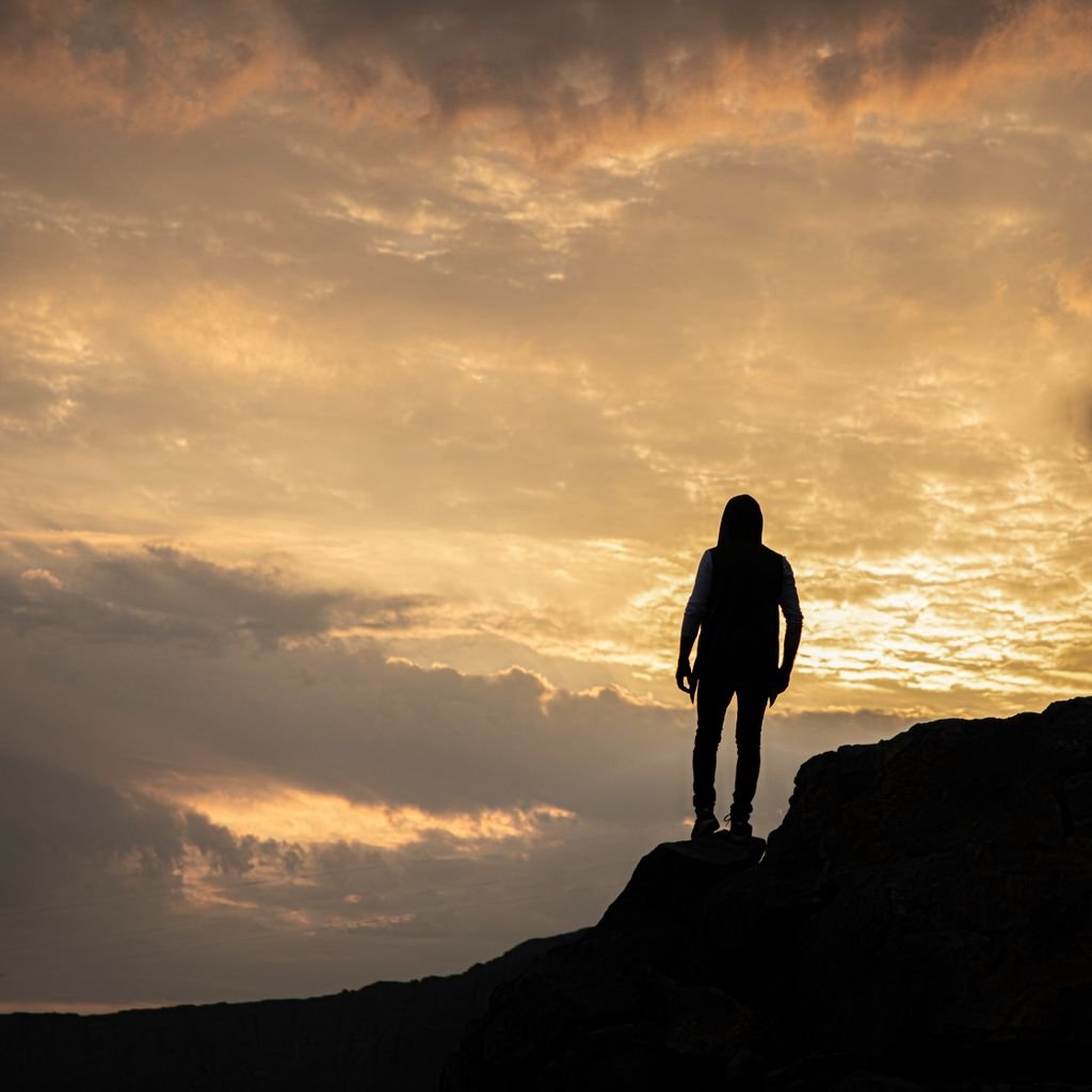 A lone hiker stands silhouetted against a dramatic sunset sky, epitomizing adventure.