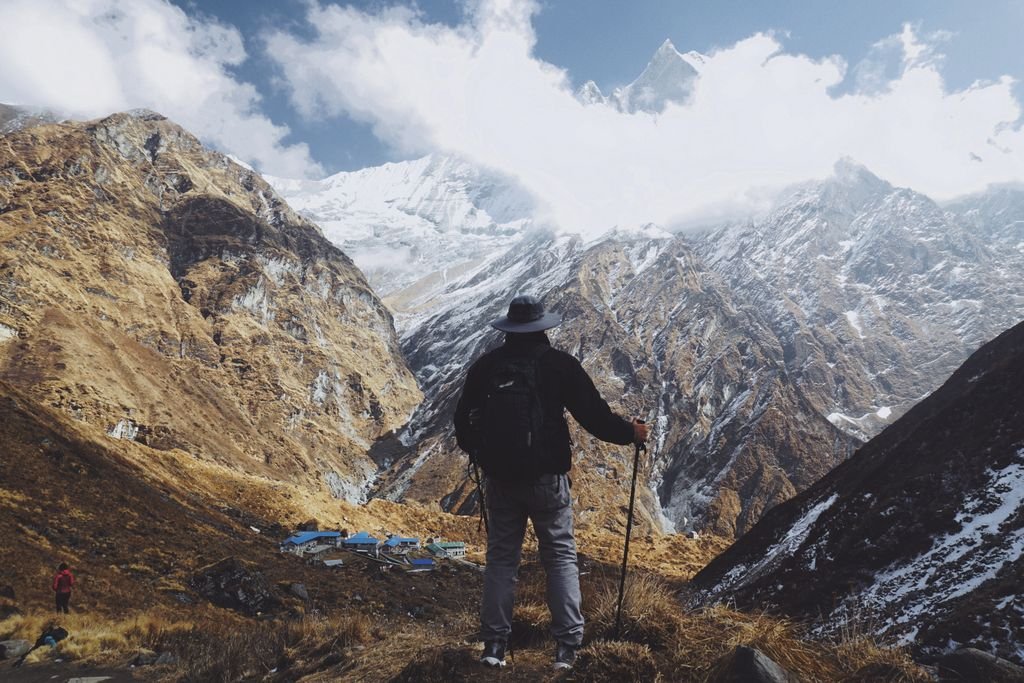 A lone hiker stands with trekking poles, admiring the breathtaking Himalayas in Nepal.
